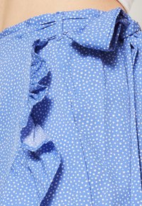 Tissu bleu à pois avec un accent volanté le long du bord, présentant un nœud noué à la taille et une texture lisse.