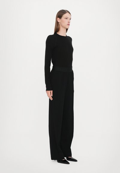Maglietta nera a maniche lunghe abbinata a pantaloni neri a gamba larga. Tessuto liscio, design minimale, e una vita aderente con eleganti scarpe nere.
