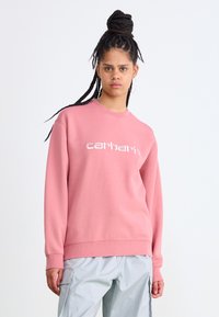 Lyserød sweatshirt med hvid "carhartt" logo, rund halsudskæring, ribbede ærmer og kant. Bæres med lysegrå cargo-bukser, der har sidelommer.