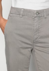Chinos en coton gris avec une coupe à plat, braguette zippée et fermeture par bouton. Ils possèdent des poches latérales obliques et des détails de couture discrets.