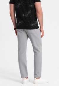 Graue Baumwollhose mit Slim-Fit und seitlichen Taschen, kombiniert mit einem schwarz gemusterten T-Shirt und weißen Sneakers.