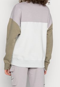 Sweatshirt med en färgblockdesign i ljuslila, vit och olivgrön; tillverkad av ett mjukt, strukturerat tyg.