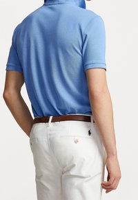 Niebieska koszulka polo z krótkim rękawem, teksturowana tkanina i kołnierzyk. Białe spodnie z brązowym skórzanym paskiem i małym ciemnym logo na tylnej kieszeni.