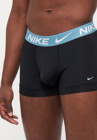 Boxeri atletici negri cu un corset de culoare albastru deschis și un logo Nike alb. Realizați dintr-un material elastic și neted pentru confort.