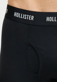 Gros plan sur une personne portant un boxer noir Hollister avec une ceinture extensible et des coutures sur la poche.