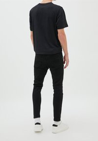 Camiseta negra de manga corta, material de algodón, combinada con jeans skinny negros. Zapatillas blancas con detalles negros. Diseño minimalista.