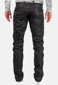 Jeans noirs avec plusieurs poches zippées, des détails de couture et une coupe slim. Portés avec des baskets blanches arborant un logo sur la semelle.