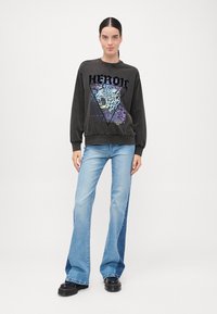 Svart hettegenser med fargerik leopardgrafikk inni en trekant, kombinert med lyseblå utsvingte jeans og svarte platå sko.