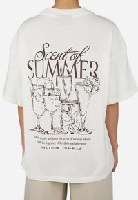 Camiseta de algodón blanca con un diseño gráfico de copas de cóctel y el texto "Scent of SUMMER" en marrón. Corte relajado con mangas anchas.