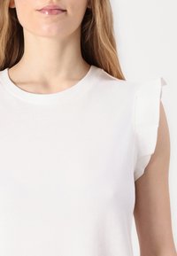 Tricou alb din bumbac, cu decolteu rotund și mâneci scurte cu volane, evidențiind o textură netedă și un design minimalist.