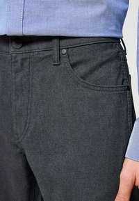 Grijze denim broek met een subtiele textuur, klassiek vijf-pocket ontwerp en zwarte knopenaccenten, gecombineerd met een lichtblauw shirt.