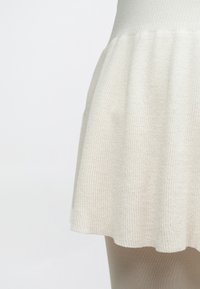 Fustă tricotată crem cu textură reiată, evazată la tiv. Materialul pare moale, completând ciorapii bej de dedesubt.