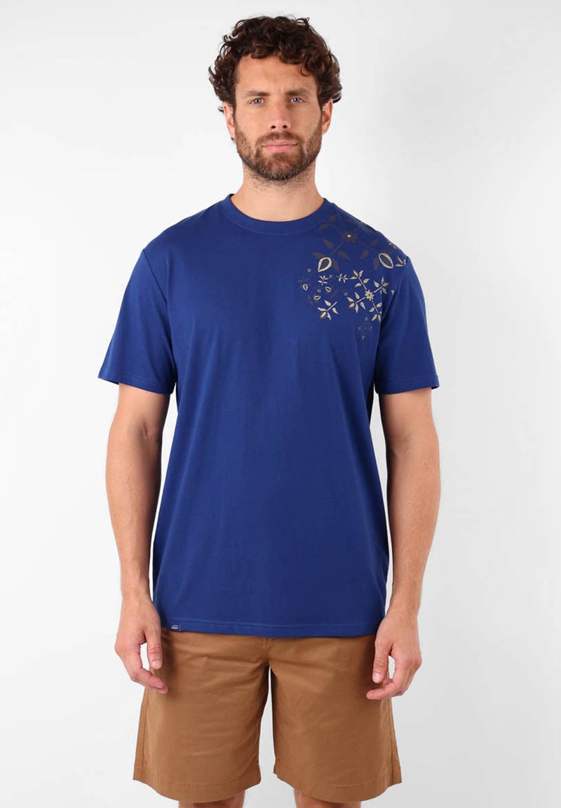 T-shirt en coton bleu avec des manches courtes, un col rond et un détail imprimé floral doré sur l'épaule gauche. Associé à un short marron.