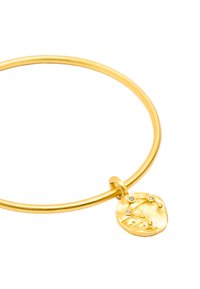 Złota bransoletka metalowa z gładką, okrągłą obręczą oraz teksturowanym charms'em z wzorem konstelacji i trzema małymi przezroczystymi kamieniami.