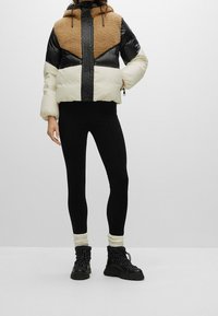 Giacca trapuntata con pannelli crema, nera e marrone; parte superiore pelosa; chiusura con zip; abbinata a leggings neri e stivali neri chunky.