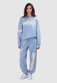 Hellblauer Trainingsanzug mit locker sitzendem Sweatshirt mit weißen Schriftzügen, passenden Jogginghosen mit gerippten Bündchen und Kordelzug an der Taille.