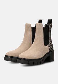 Beige mokkanahkasaappaat mustilla elastisilla paneeleilla ja teksturoidulla mustalla yksityiskohdalla. Tukeva musta korko, jossa on uritettu pohja. Klassinen Chelsea-malli.