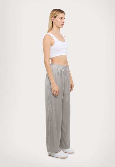 Top blanc court avec des bretelles larges, associé à un pantalon léger gris clair en satin et des baskets blanches. Présenté sur un mannequin de profil.