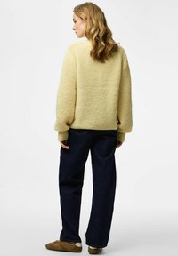 Maglione giallo lavorato a maglia con una finitura testurizzata, maniche larghe, indossato sopra jeans blu scuro a gamba larga e sneakers marroni.