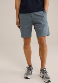 Svetlo modri bombažni kratki hlače z stranskimi žepi, sproščenega kroja in zavihanimi robovi, v kombinaciji s sivo športno obutvijo z mrežastimi in usnjenimi detajli.