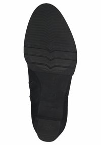 Schwarze Gummisohle mit strukturierten Mustern, ausgestattet mit Zickzackprofilen für besseren Halt und einem glatten, abgerundeten Fersenbereich.