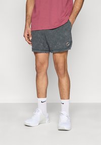 Σκούρα γκρι, υφασμάτινα σορτς με ελαστική ζώνη μέσης και πλαϊνές τσέπες, με ένα μικρό λογότυπο. Συνδυασμένα με λευκά αθλητικά παπούτσια και κάλτσες.