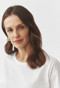 Hvid bomulds T-shirt med rund halsudskæring, båret af en person med mellemlangt bølget brunt hår. Enkel og glat stoftekstur.