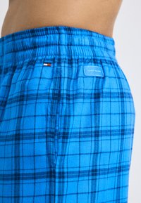 Blauwe geruite broek van zachte stof; voorzien van een elastische tailleband, met een logo label en een kleine accenten in rood en wit.