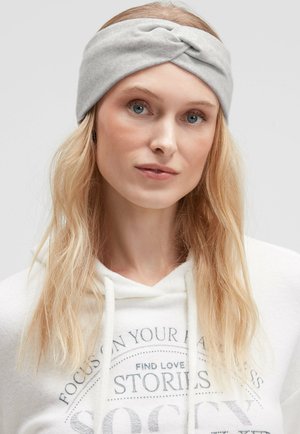 Light gray, knitted headband with a twisted front design. Soft texture, suitable for warm wear. Paired with a white hoodie featuring printed text.