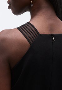 Mustast kangast voolujooneline rõivas, millel on tagaküljel mitu õhukest musta rihma ning peen tõmblukuelement.