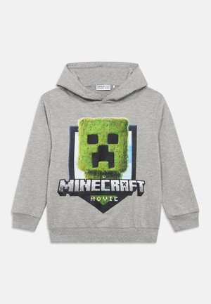 Szürke kapucnis sweatshirt zöld blokk karakter grafikával, pajzs körül, és "A Minecraft Film" felirat erős fekete és fehér betűkkel.