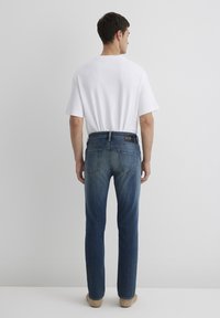 Jeans in denim azzurro chiaro, aderenti, con taglio dritto, tasche posteriori e etichetta nera. Abbinati a una t-shirt bianca dal taglio ampio.