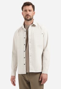 Lichtbeige overhemd met knopen, gemaakt van katoen, met twee borstzakken, lange mouwen en een relaxte pasvorm. Het overhemd heeft grijze knopen.