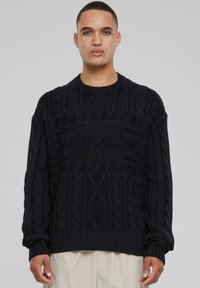 Pull en tricot noir avec des motifs texturés, col rond et poignets en côtes, arborant une coupe décontractée et un tissu épais et chaud.