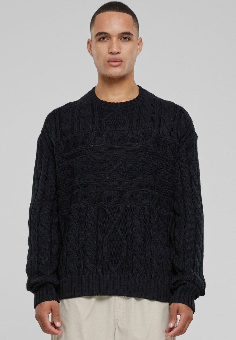 Pull en tricot noir avec des motifs texturés, col rond et poignets en côtes, arborant une coupe décontractée et un tissu épais et chaud.