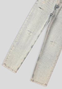 Jeans in denim strappato di colore azzurro chiaro distesi, che mostrano dettagli strappati su entrambe le gambe e cuciture visibili.