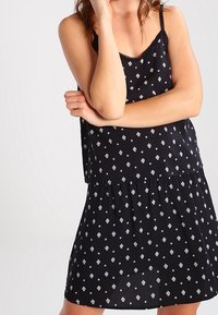 Abito nero caratterizzato da una vestibilità ampia, spalline regolabili e gonna arricciata. Il tessuto presenta un motivo geometrico bianco su tutta la superficie.