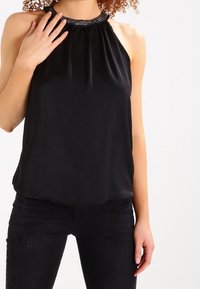 Svart halterneck-top med en pärlbroderad krage, lätt tyg, löst skuren och slät yta, i kombination med mörka jeans.