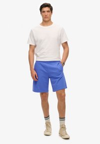 Herenoutfit met een witte katoenen T-shirt met korte mouwen en blauwe stretchshorts, met een soepele textuur en elastische tailleband.