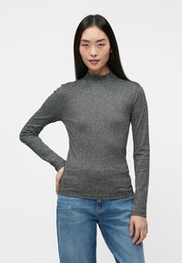 Langærmet, højhalset grå ribbet top med en struktureret stof, tætsiddende design og subtil glans. Kombineret med lyseblå denimjeans.