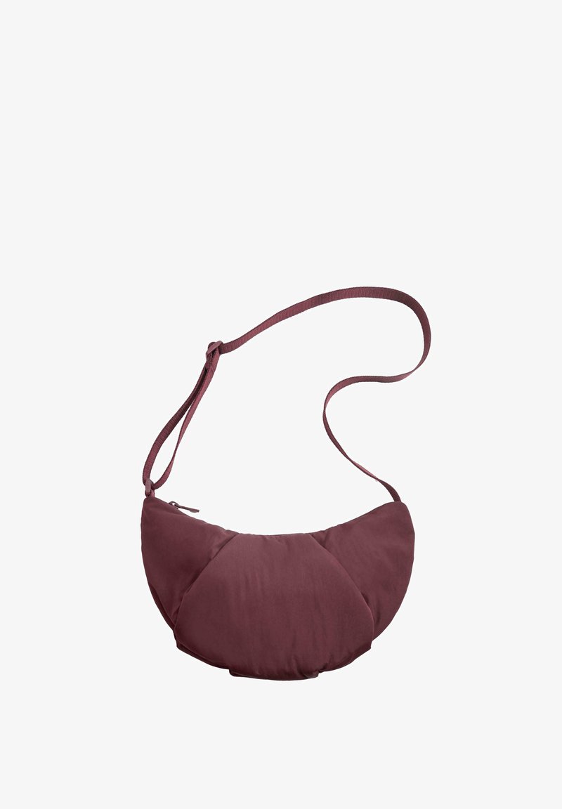 Burgundska crossbody torba za rame sa zaobljenim oblikom, izrađena od mekog, teksturiranog materijala, sa zatvaranjem na zip i tankim podesivim remenom.