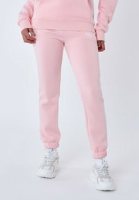 Pantalones de chándal rosa claro fabricados con un tejido suave, con un diseño ajustado, puños elásticos y un pequeño logo blanco en el muslo.
