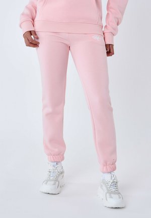 Pantalones de chándal rosa claro fabricados con un tejido suave, con un diseño ajustado, puños elásticos y un pequeño logo blanco en el muslo.