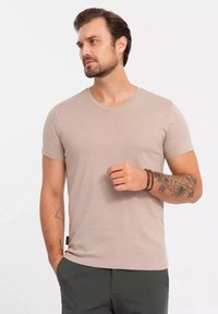 Camiseta de manga corta en color beige claro con escote en forma de V, fabricada en material suave. Presenta un diseño ajustado y costuras mínimas.