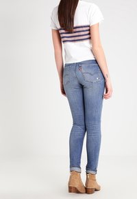 Camiseta blanca con un diseño de espalda a rayas, combinada con jeans ajustados azules y botas de tobillo marrón claro con tacón de madera.