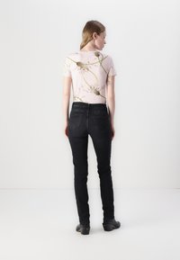 Top floral rosa claro com mangas curtas, combinado com jeans pretos justos, com bolsos traseiros e uma textura suave. Tamancos pretos de salto.