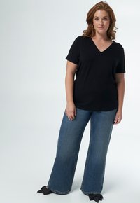 T-shirt noir à col en V associé à un jean en denim bleu à jambes larges avec des ourlets effilochés et des nœuds sur des chaussures noires à enfiler.