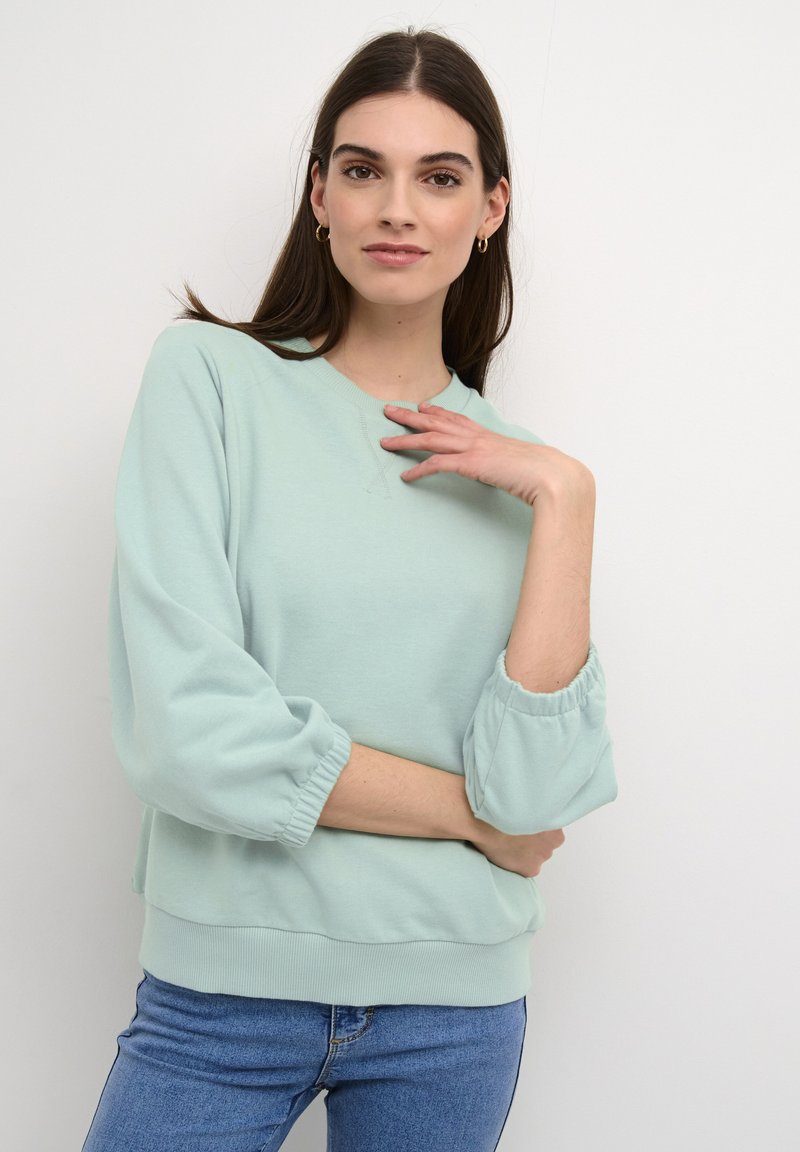 Kerge mündi roheline sweatshirt, millel on elastsed kummist varrukad, ümmargune kaelus ja soonikkoes äär. Omab pehmet tekstuuriga kangast.