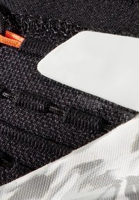 Schwarzer Stoff mit einer strukturierten Oberfläche, der ein orangefarbenes Akzent sowie ein weißes glattes Panel aufweist. Sichtbare Nähte und eine gemusterte Sohlenkante sind ebenfalls enthalten.