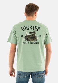 Lichtgroene katoenen T-shirt met een zwarte slangafdruk en "Dickies" tekst op de achterkant, ronde halslijn en korte mouwen.